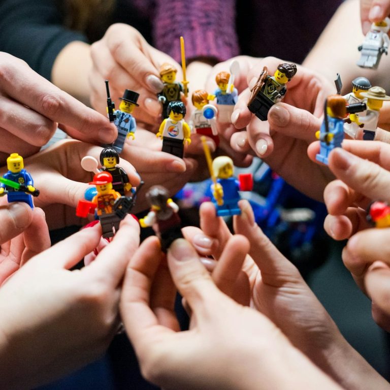 Das sind wir Hände halten zahlreiche LEGO-Figuren in einer versammelten Runde.