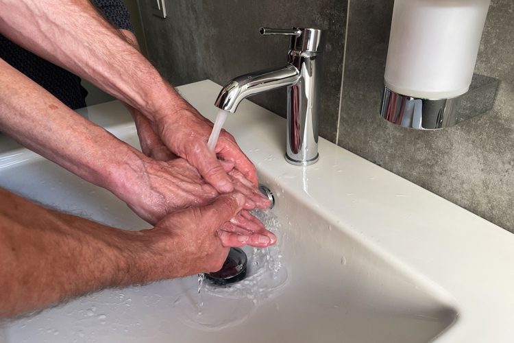 Zwei Hände waschen zwei ältere Hände unter einem Wasserhahn in einem Waschbecken.