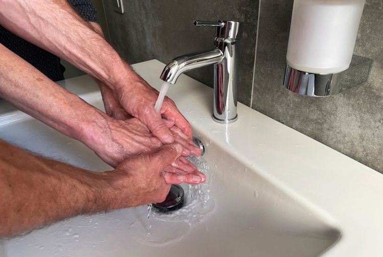 Grundpflege Zwei Hände waschen zwei ältere Hände unter einem Wasserhahn in einem Waschbecken.