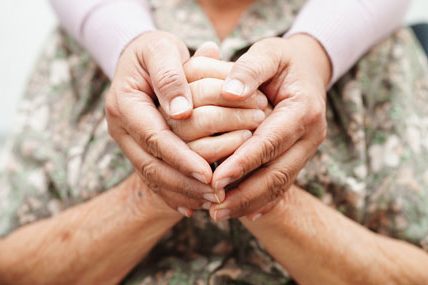 Zwei Hände, die zwei ältere Hände umschließen. Das Bild symbolisiert Unterstützung und Fürsorge