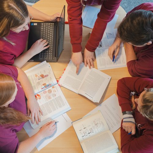 Ausbildung Gruppengespräch am Tisch mit Büchern und Laptop, Schüler zeigen auf Seiten.