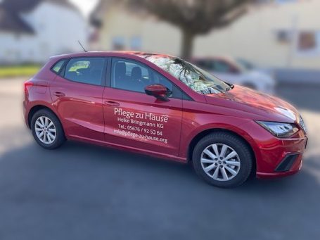 Roter Kompaktwagen mit Aufschrift des Pflegedienstes auf der Seite, geparkt auf einem Parkplatz.