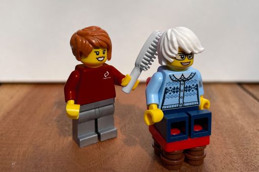 Pflegehilfskräfte Zwei LEGO-Figuren: Eine Figur mit Haarbürste in der Hand und eine Figur mit frisiertem, weißem Haar.