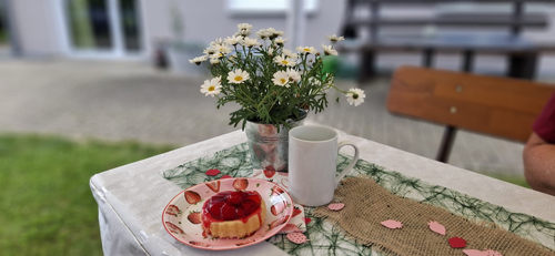 Gedeck Tischgedeck mit Erdbeertorte, Blumenstrauß und Tasse in einem Garten.