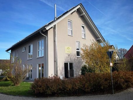 Gartenbereich Weinrotes Wohnhaus mit grüner Bepflanzung und Holzschuppen im Vordergrund.