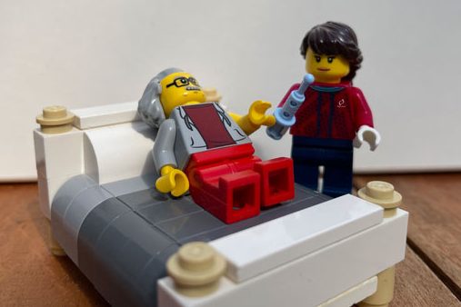 Pflegefachkräfte Ein LEGO-Figur steht mit einer Spritze in der Hand neben einer anderen, die auf einem Bett liegt.