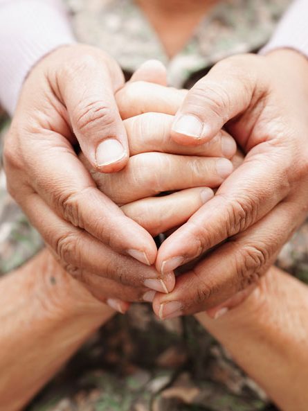 Zwei Hände, die zwei ältere Hände umschließen. Das Bild symbolisiert Unterstützung und Fürsorge.