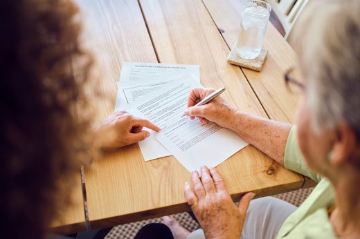 Beratung Zwei Personen, eine ältere Frau und eine jüngere Person, die gemeinsam Dokumente ausfüllen.