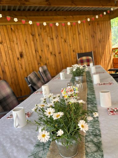 Tischdeko Erdbeerfest Ein gedeckter Tisch mit Blumen und Kerzen, umgeben von Holzdekor und Lichterketten.